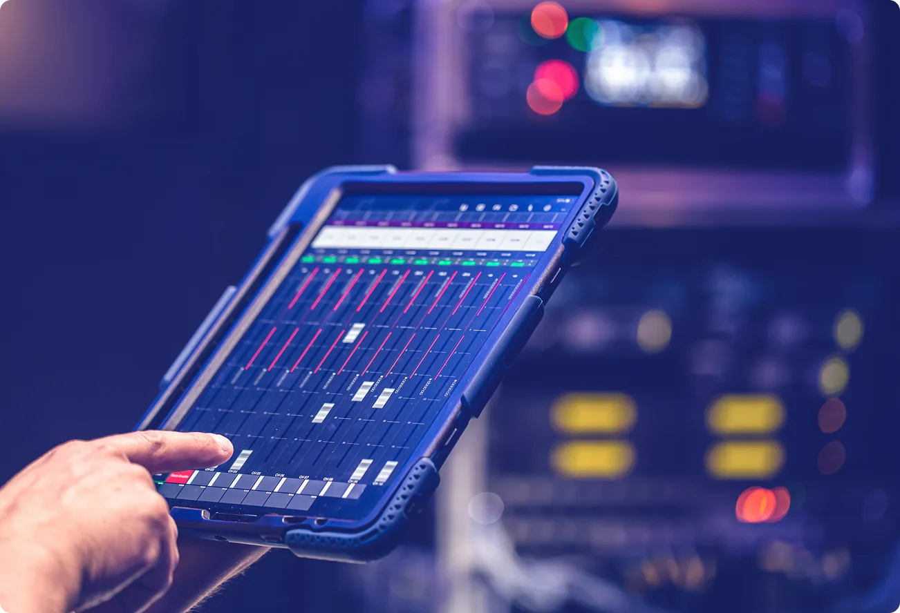 Hand adjusting audio mixer app on a tablet in front of rack gear.
